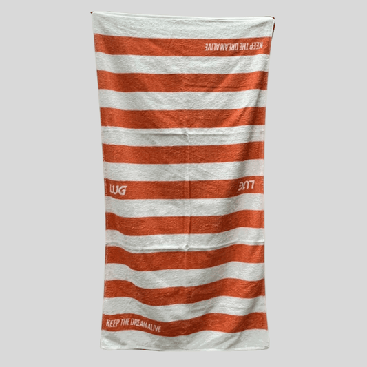 A striped cotton towel with orange and white colors, featuring the 'LUG' logo and 'KEEP THE DREAM ALIVE'.